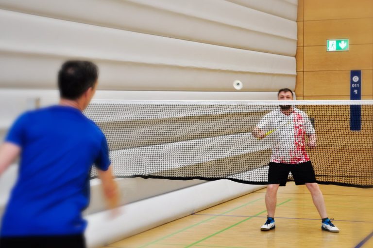 Trainingssituation zweier Spieler Zwei Spieler in einer Sporthalle spielen sich den Badmintonball über das Netz zu.
