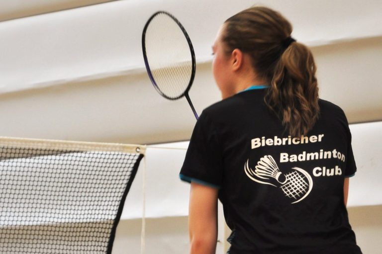 Junge Spielerin mit Schläger Junge Spielerin konzentriert mit Badmintonschläger am Netz in einer Sporthalle.
